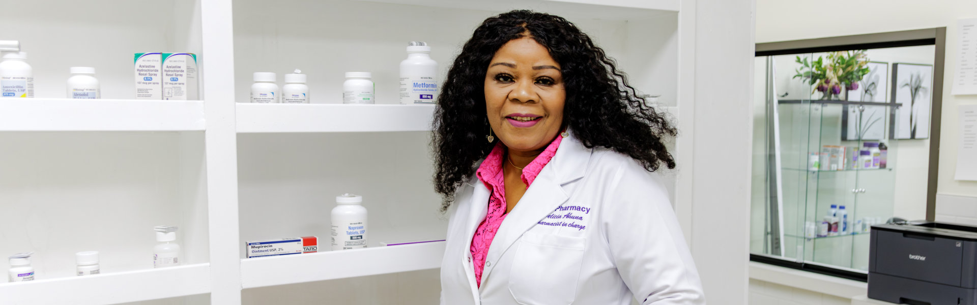 pharmacist smiling in front of a shelf of medicine bottles